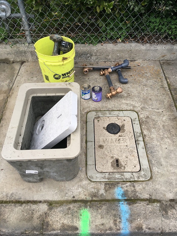 Pipes, sealant, new water meter box sitting on sidewalk