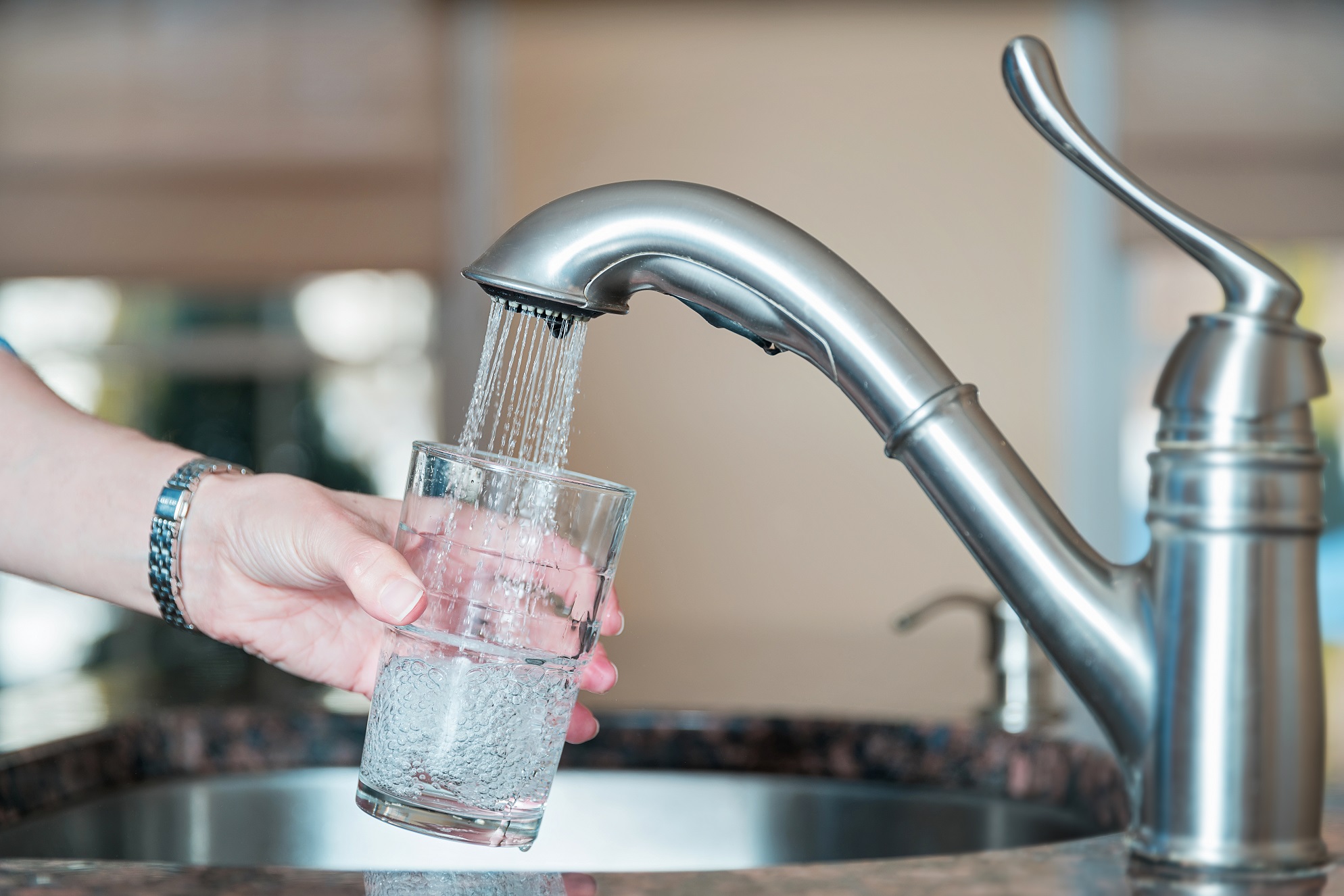 a woman's hand holding a clear glass beneath a running kitchen tap